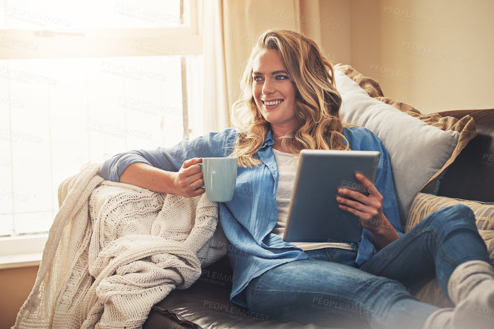 Buy stock photo Shot of a relaxed young woman having coffee and using a digital tablet on the sofa at home