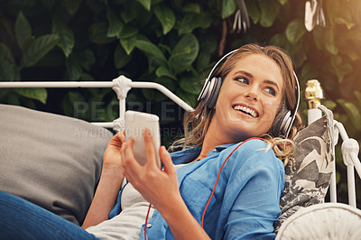 Buy stock photo Shot of a young woman using headphones with her smartphone while relaxing in the garden at home