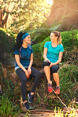 Buy stock photo Shot of two sporty young women taking a break while out exercising in nature