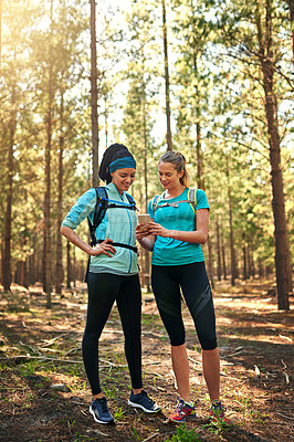 Buy stock photo Shot of two sporty young woman using a cellphone while out in nature