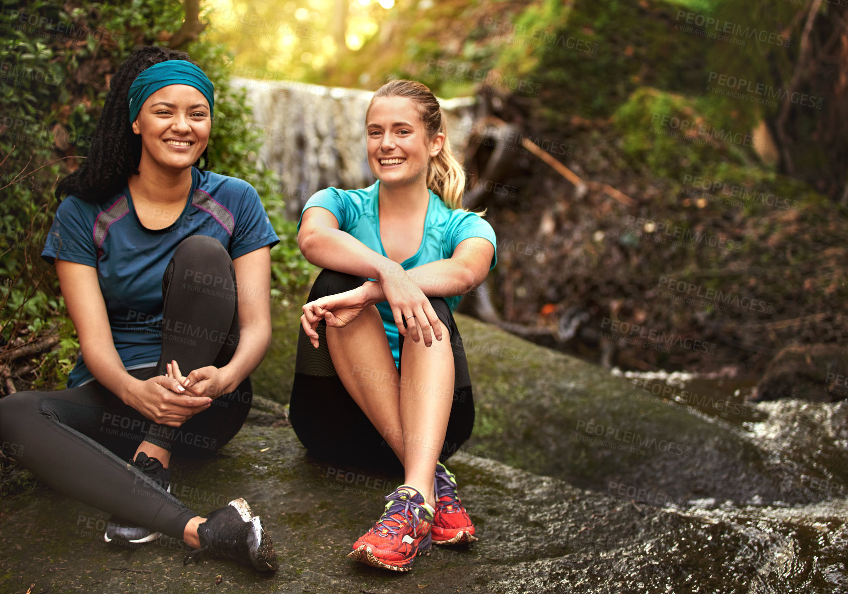 Buy stock photo Shot of two sporty young women taking a break while out exercising in nature