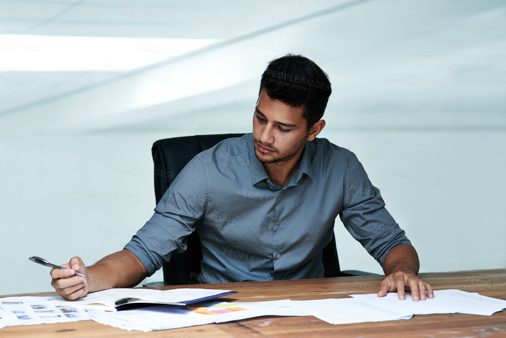 Buy stock photo Cropped shot of a handsome young businessman doing paperwork while working in a modern office