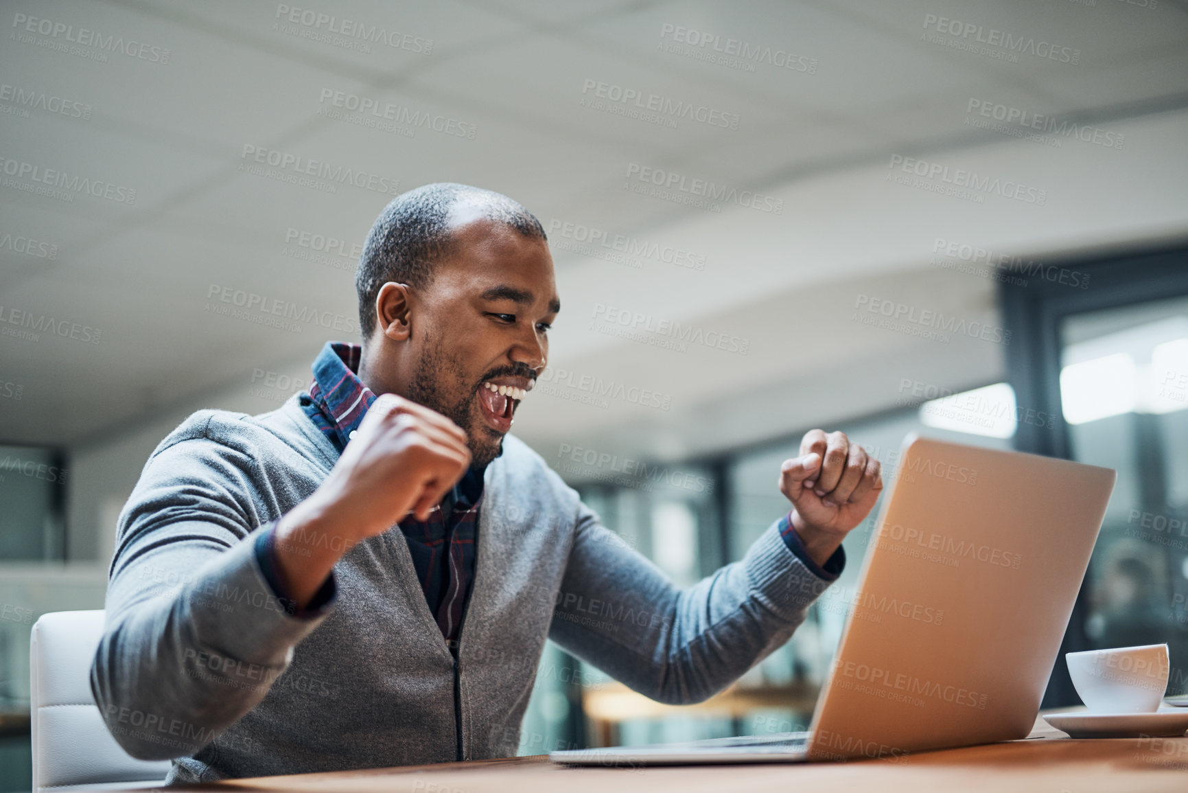 Buy stock photo Shot of a cheerful young businessman celebrating with his fists clinched while working in his office