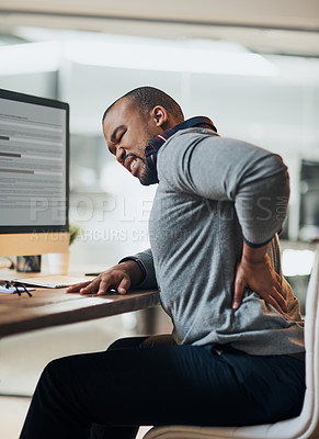 Buy stock photo Shot of a young businessman suffering from a backache while working at his desk in his office