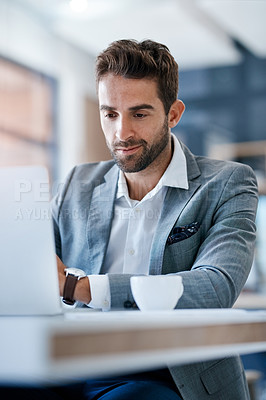 Buy stock photo Cropped shot of a handsome young businessman using a laptop at his desk in a modern office
