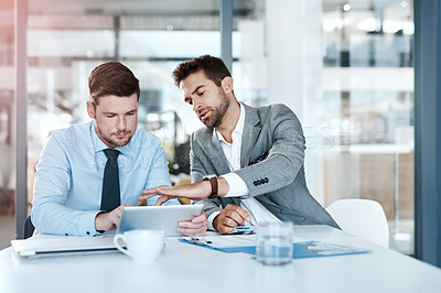 Buy stock photo Cropped shot of two young businessmen using a digital tablet while going through paperwork together in a modern office