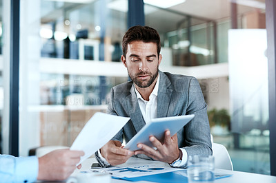 Buy stock photo Cropped shot of two businessmen using a digital tablet while going through paperwork together in a modern office