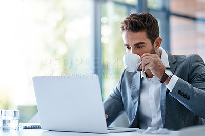 Buy stock photo Cropped shot of a handsome young businessman using a laptop and having coffee at his desk in a modern office