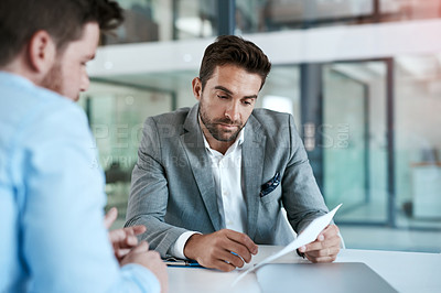 Buy stock photo Cropped shot of two young businessmen using a laptop while going through paperwork together in a modern office
