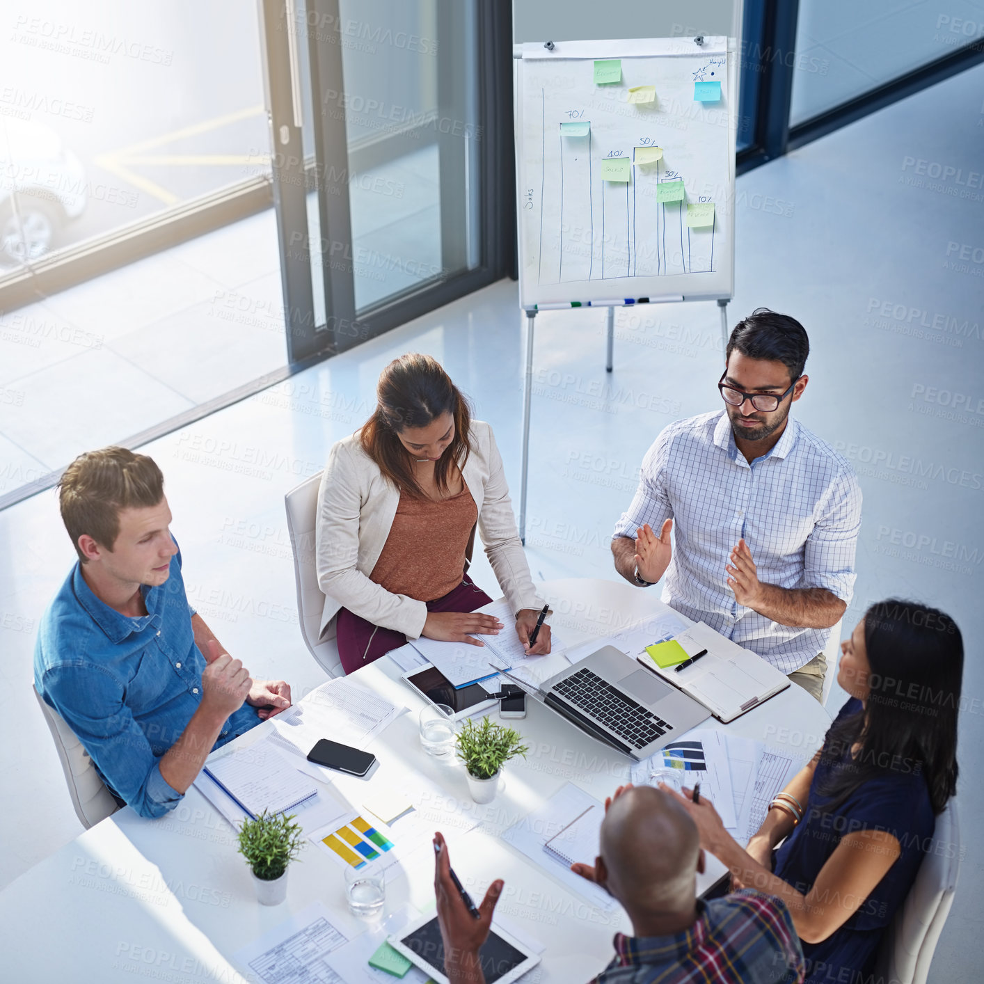 Buy stock photo High angle shot of a group of young businesspeople having a meeting together around a table in a modern office
