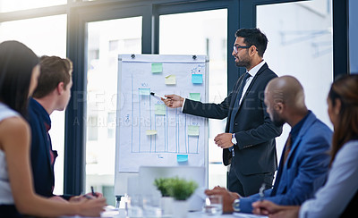 Buy stock photo Shot of a young businessman giving a demonstration on a white board to his colleagues in a modern office