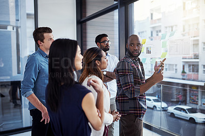 Buy stock photo Shot of a young businessman giving a demonstration on a glass wall to his colleagues in a modern office