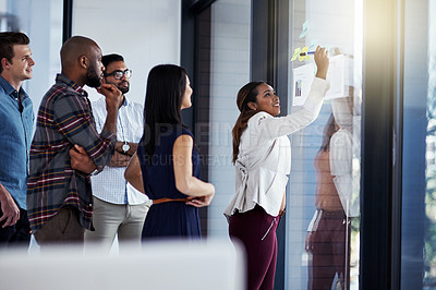 Buy stock photo Shot of a young businesswoman giving a demonstration on a glass wall to her colleagues in a modern office