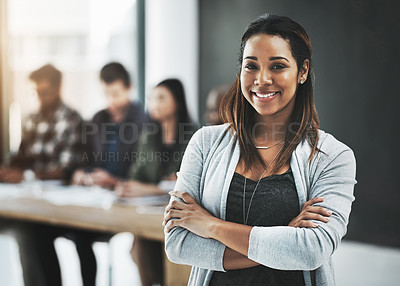 Buy stock photo Portrait of a cheerful businesswoman posing with her arms folded in a modern office with her colleagues in the background
