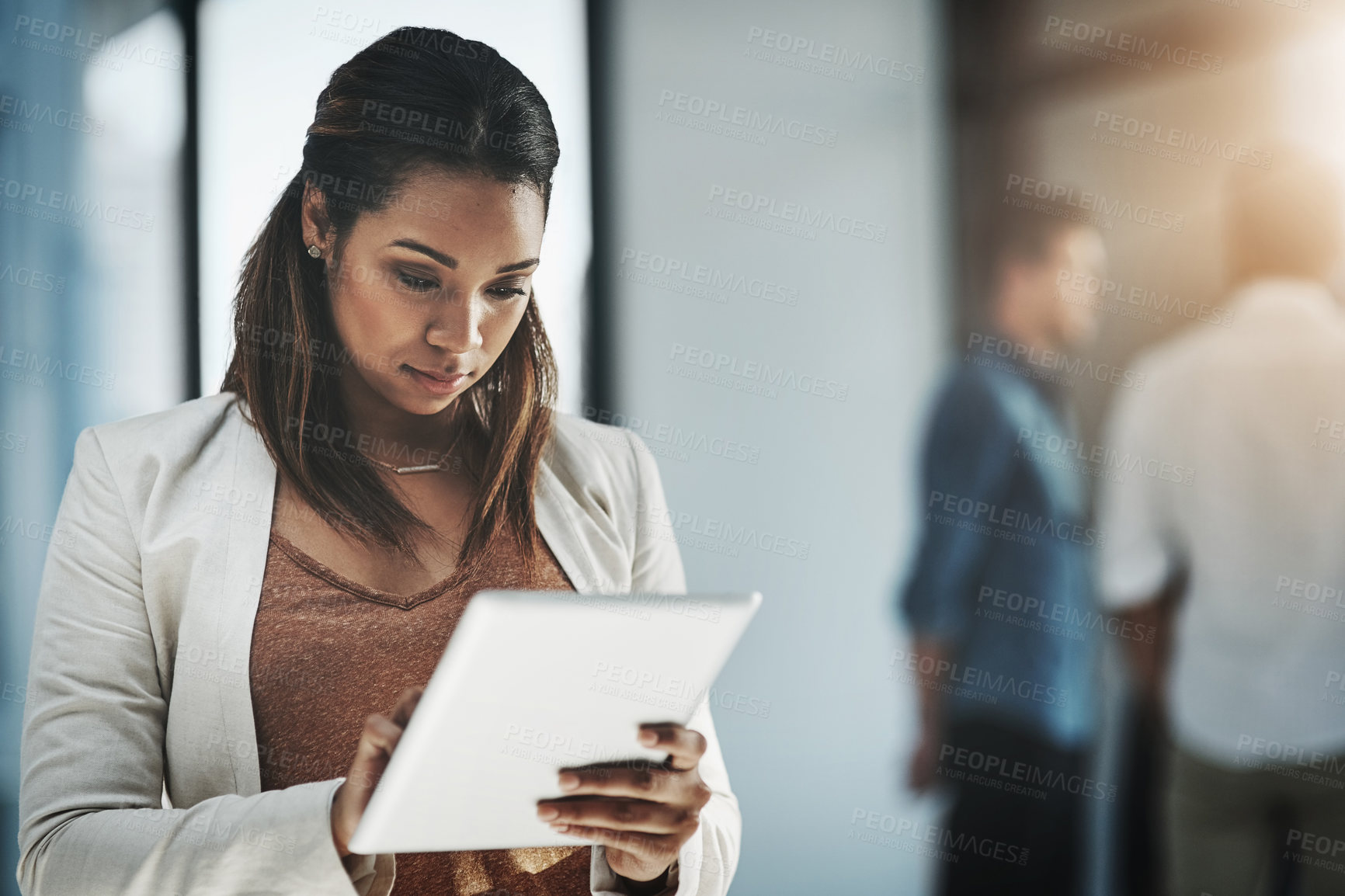 Buy stock photo Shot of a young businesswoman using her digital tablet in a modern office with her colleagues in the background