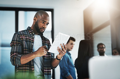 Buy stock photo Shot of a young businessman using his digital tablet in a modern office with his colleagues in the background
