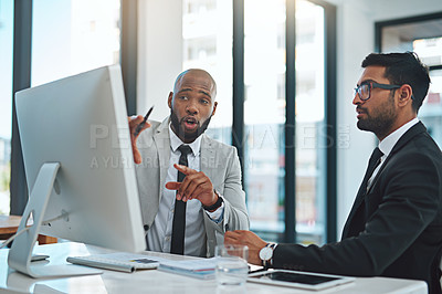 Buy stock photo Cropped shot of two young businessmen having a discussion while working on a computer in a modern office