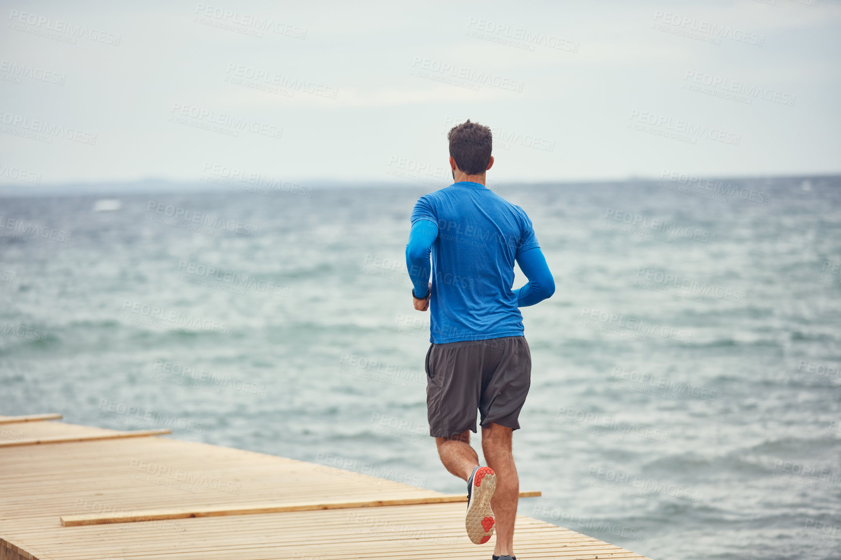 Buy stock photo Rearview shot of a sporty man out running by the seaside