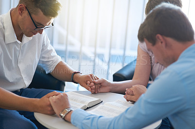 Buy stock photo Shot of a group of young businesspeople holding hands while deep in prayer at work