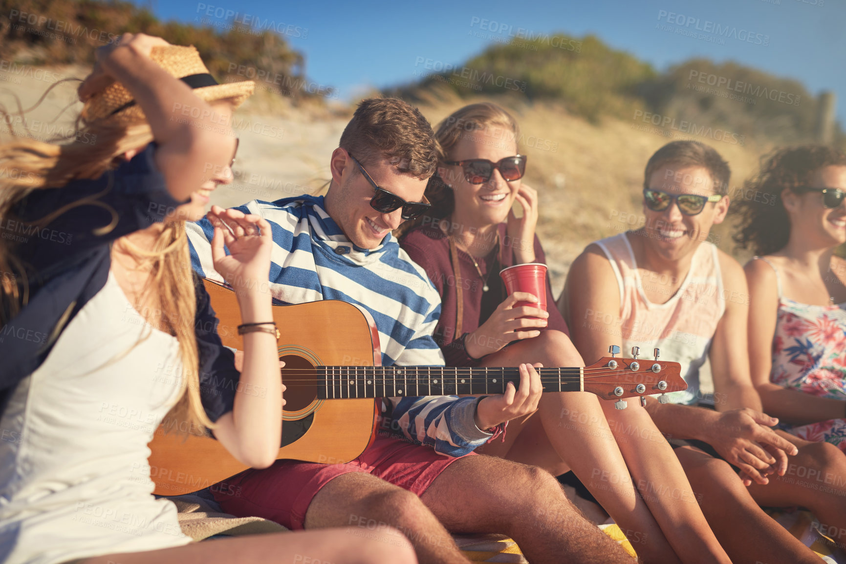 Buy stock photo Cropped shot of a handsome young man playing a guitar for his friends on a summer's day at the beach