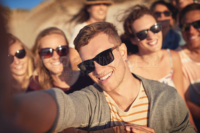 Buy stock photo Cropped portrait of a handsome young man taking a selfie with his friends at the beach
