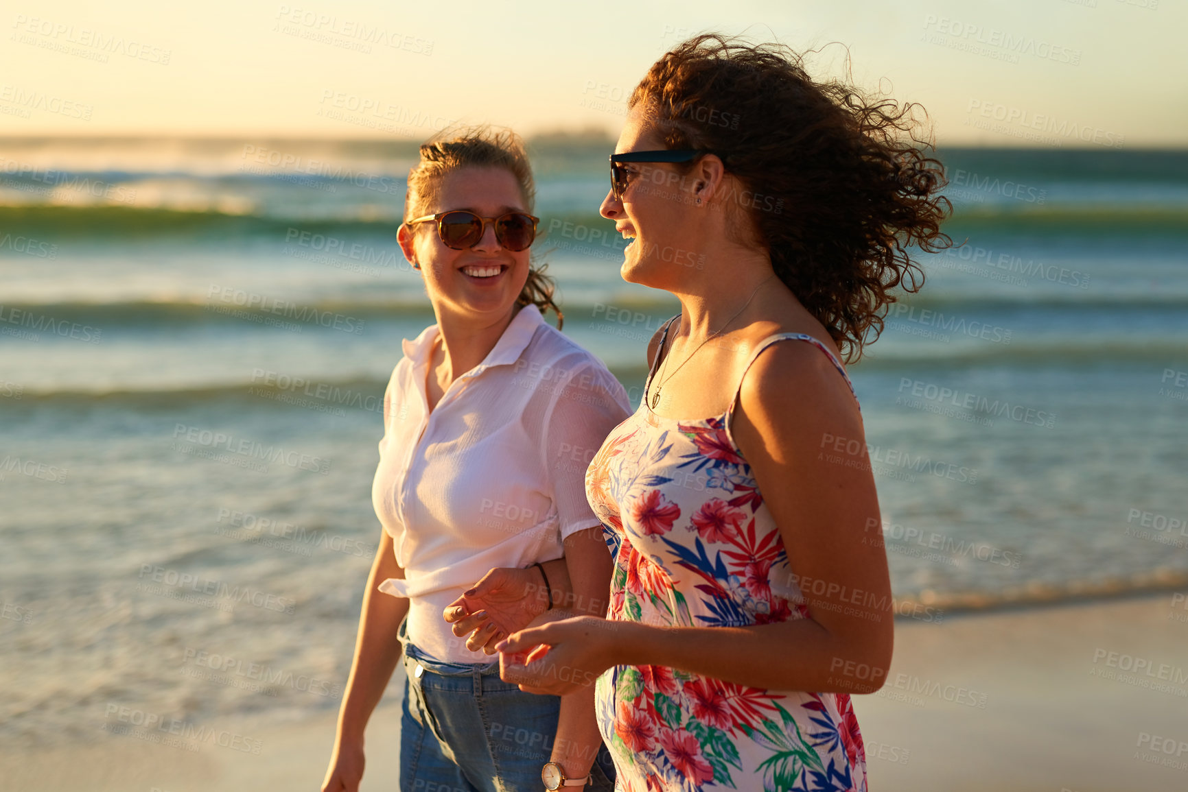 Buy stock photo Cropped shot of two attractive young girlfriends having a chat while strolling on the beach