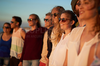 Buy stock photo Cropped shot of a group of young friends standing together on the beach during the day