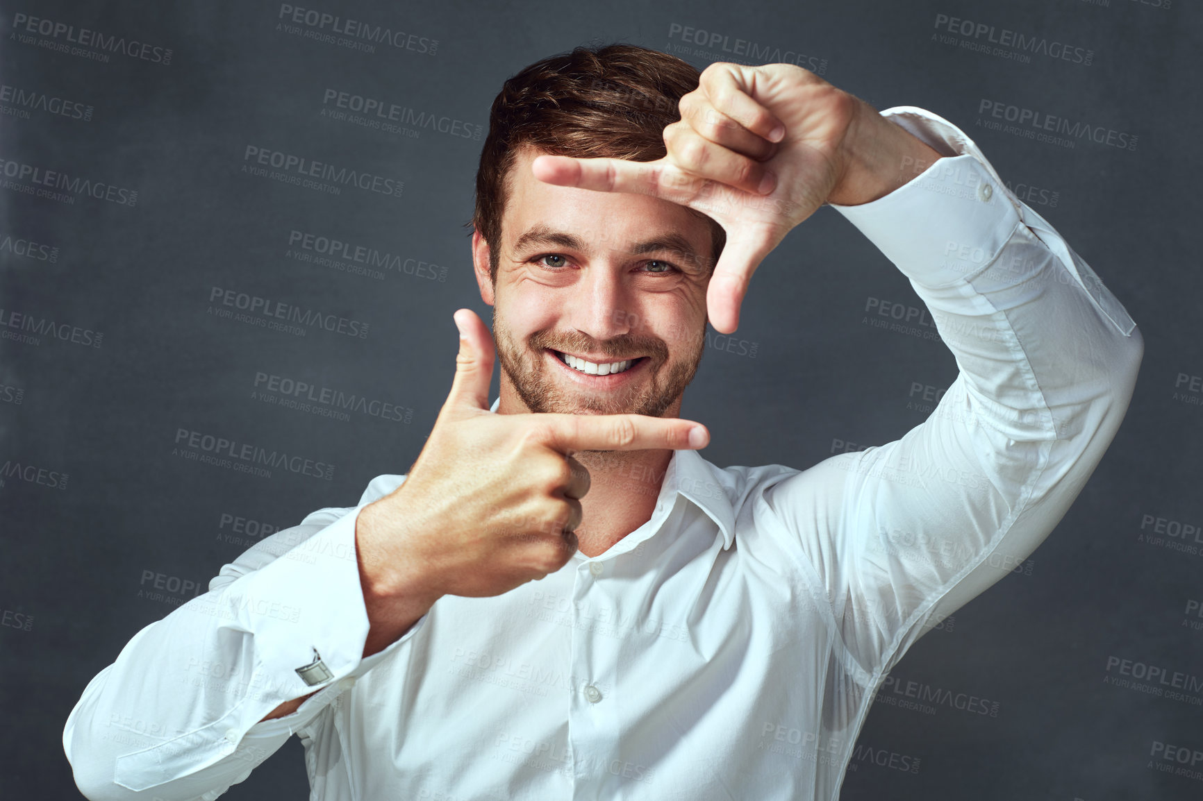 Buy stock photo Studio portrait of a handsome young man framing with his fingers against a dark background
