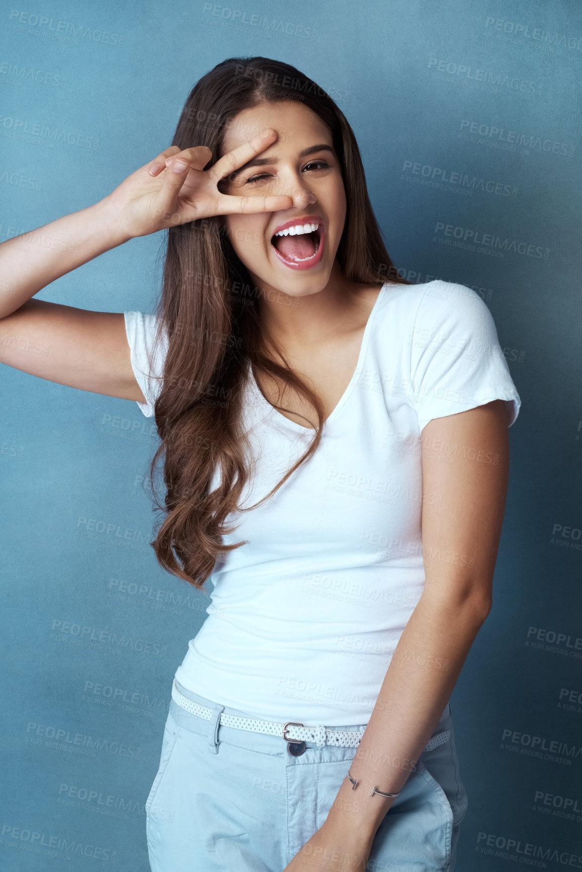 Buy stock photo Studio shot of an attractive young woman looking through her fingers against a blue background