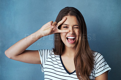 Buy stock photo Studio shot of an attractive young woman looking through her fingers against a blue background