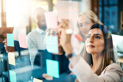Buy stock photo Shot of a group of businesswomen arranging sticky notes on a glass wall in a modern office