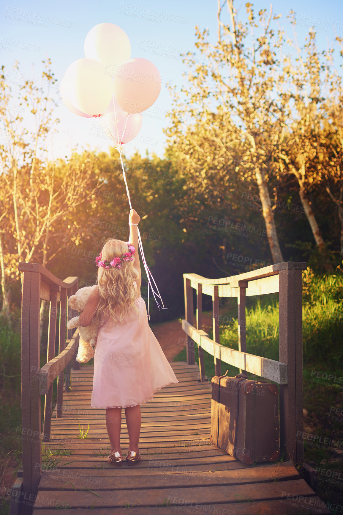 Buy stock photo Back, bridge and girl with balloons, playing and creativity for festival, carnival and celebration. Outdoor, childhood and kid with fantasy, carefree and party with adventure, nature and luggage