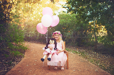 Buy stock photo Shot of a happy little girl sitting and waiting with a doll and balloons in the middle of a dirt road