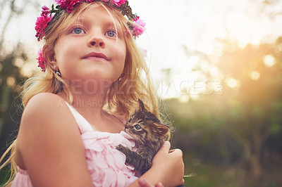 Buy stock photo Shot of a little girl holding a kitten and looking into the distance while standing outside in nature