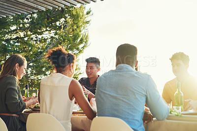 Buy stock photo Rearview shot of a group of friends enjoying a meal and drinks  together around a table at a gathering outdoors