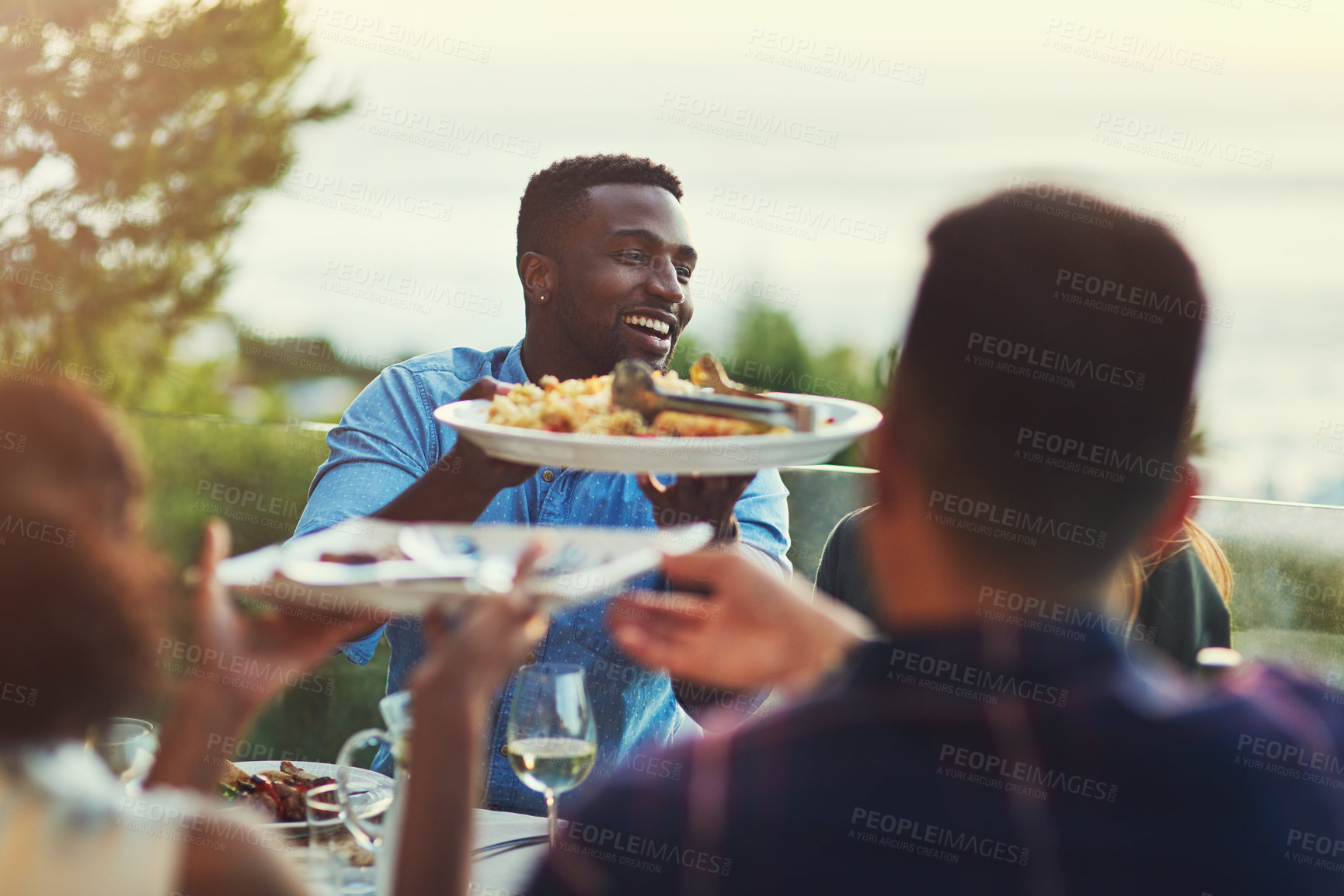 Buy stock photo Shot of a handsome young man passing a plate of pasta around at a gathering with friends outdoors