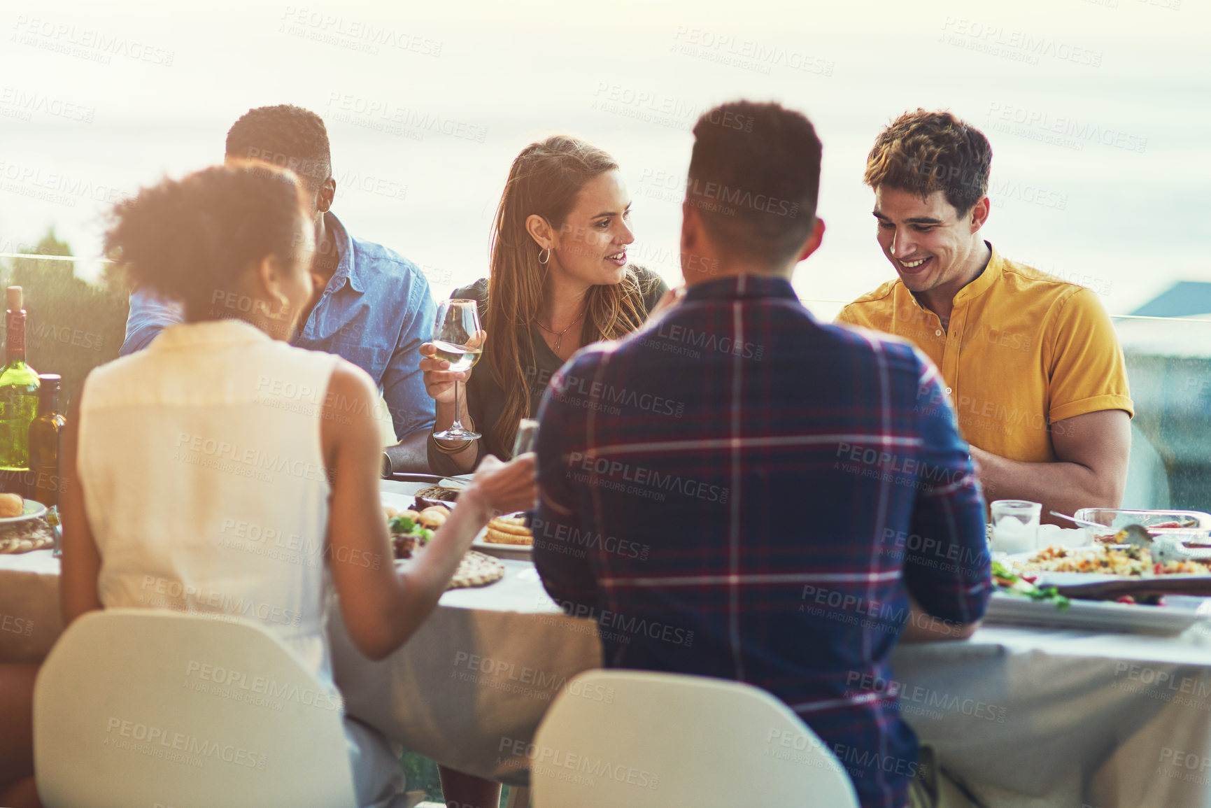 Buy stock photo Shot of a group of friends enjoying a meal and drinks together around a table at a gathering outdoors