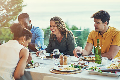 Buy stock photo Shot of a group of friends enjoying a meal and drinks  together around a table at a gathering outdoors
