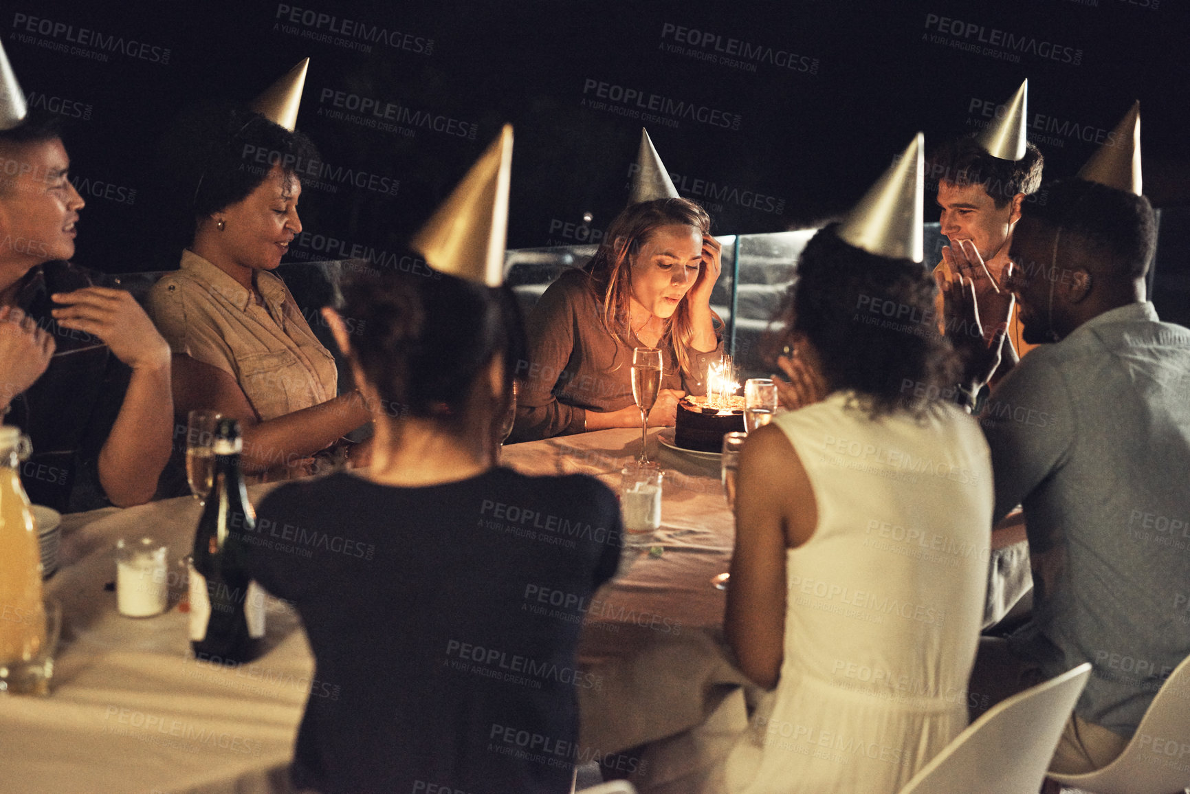 Buy stock photo Shot of a beautiful young woman blowing the candles on her birthday cake at a evening gathering with friends