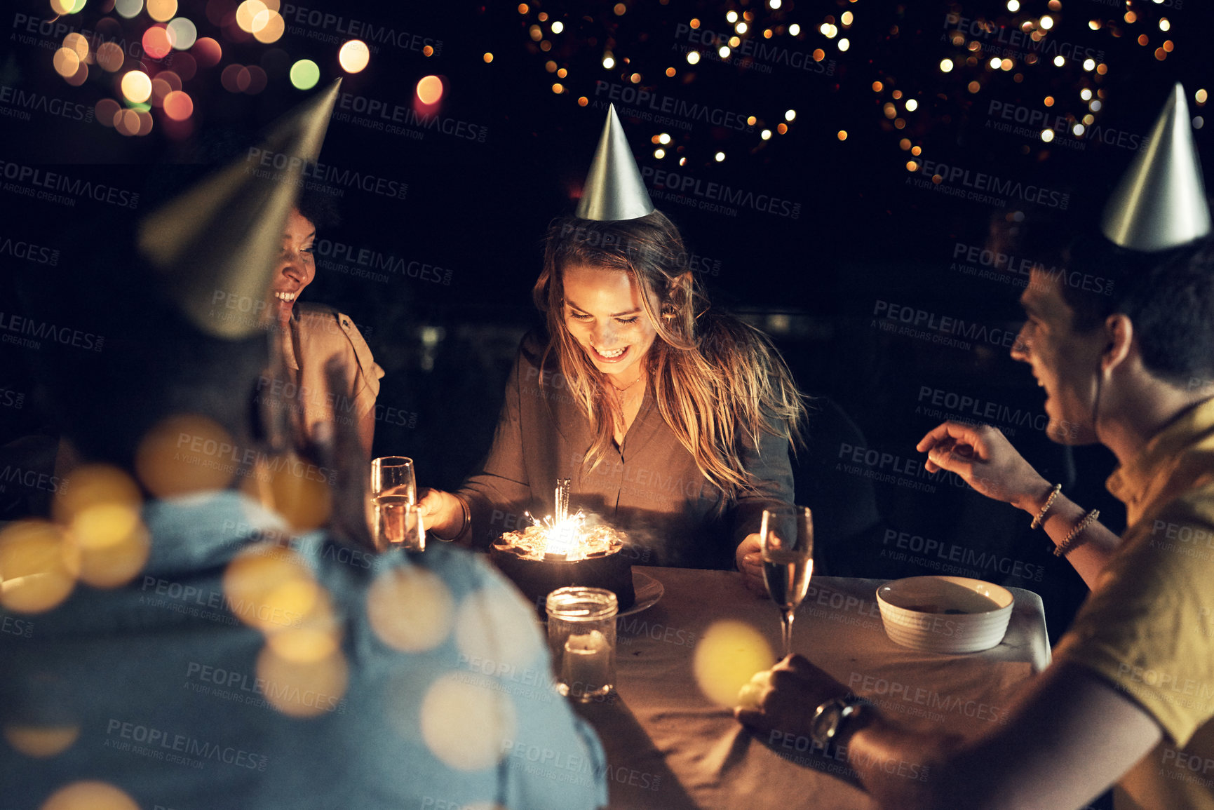 Buy stock photo Shot of a group of friends celebrating a birthday together around a table at a gathering outdoors in the evening