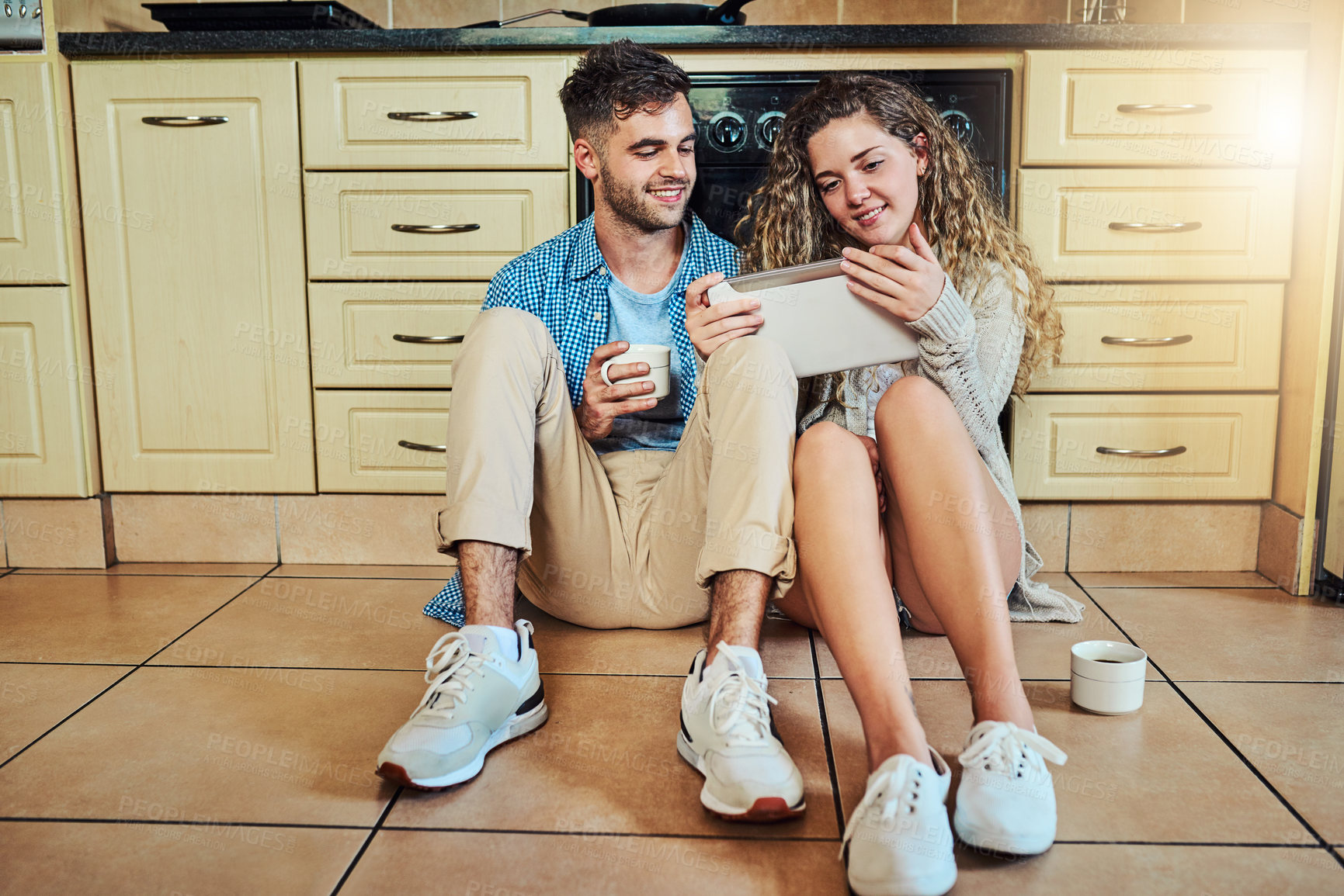 Buy stock photo Shot of a couple using a digital tablet while sitting on their kitchen floor
