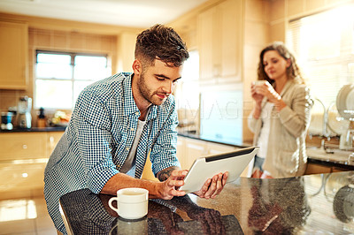 Buy stock photo Shot of a young man using a digital tablet with his girlfriend standing in the background