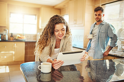 Buy stock photo Shot of a young woman using a digital tablet with her boyfriend standing in the background