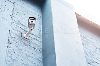 Buy stock photo Low angle shot of a security camera mounted on a wall outside a building