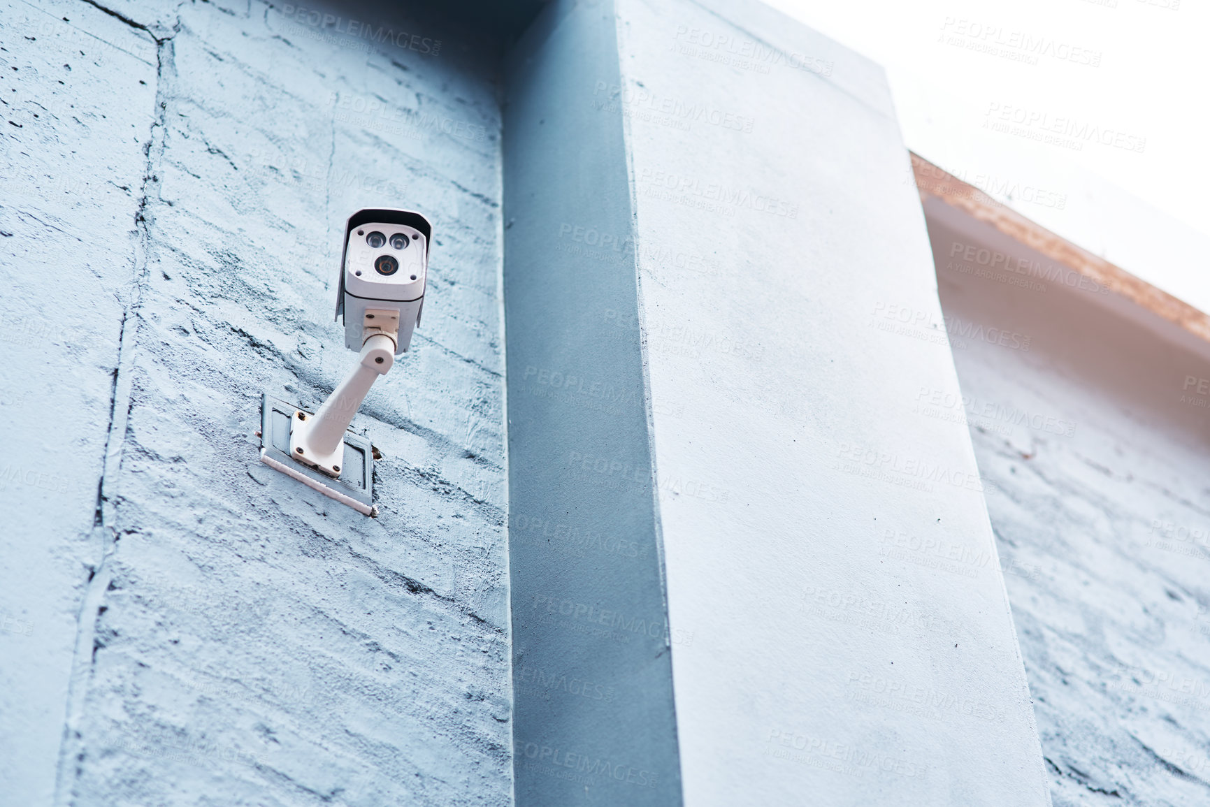 Buy stock photo Low angle shot of a security camera mounted on a wall outside a building