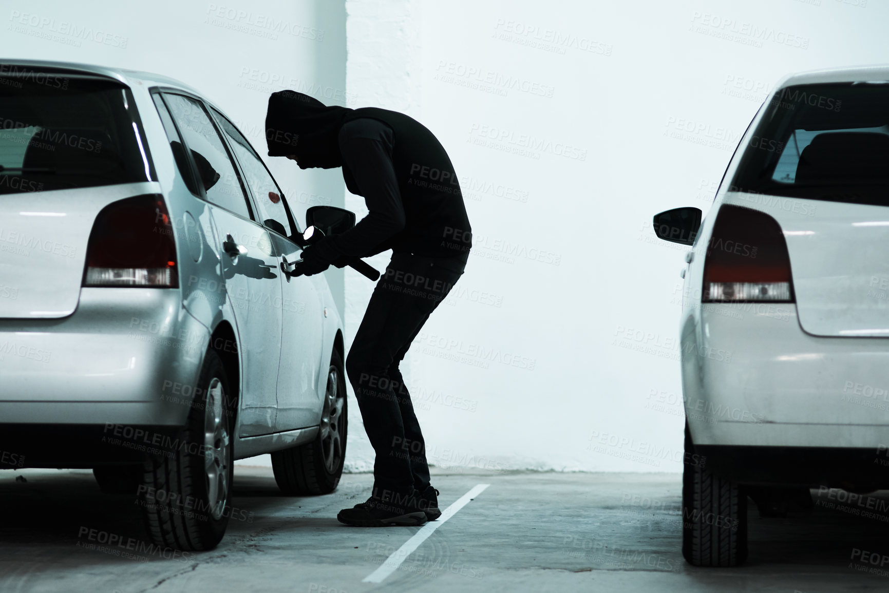 Buy stock photo Full length shot of a masked criminal picking the lock of a car door inside a parking lot