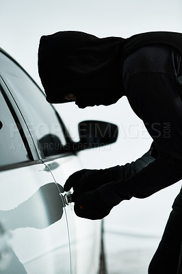 Buy stock photo Shot of a masked criminal picking the lock of a car door inside a parking lot