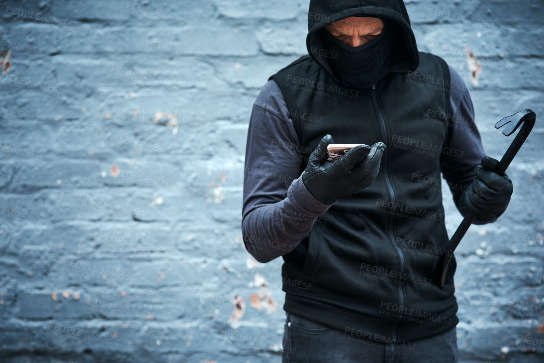 Buy stock photo Thief, phone and crime outdoor for danger, illegal and burglar with hoodie, mask and steel bar as weapon. Criminal, smartphone and warning by wall for security camera, time and mobile call as alibi