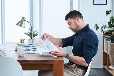 Buy stock photo Shot of a handsome mature businessman looking through some paperwork while sitting in his office