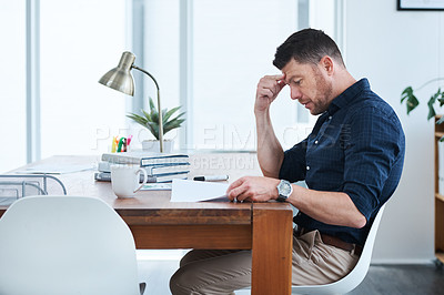 Buy stock photo Shot of a handsome mature businessman looking through some paperwork while sitting in his office